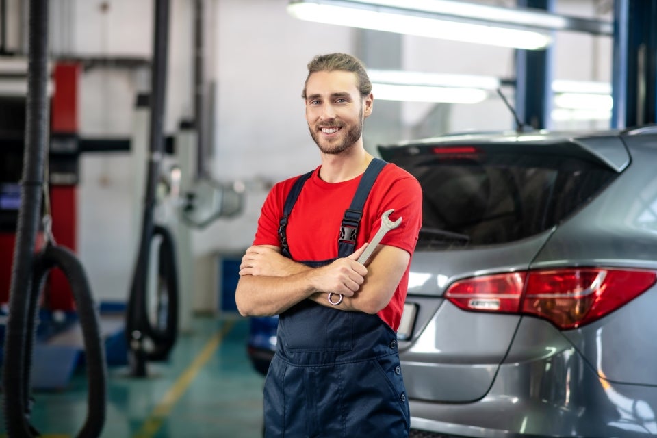 A technician standing with a spanner in hand in an auto repair shop.