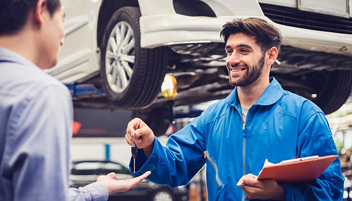 A smiling mechanic hands car keys to a customer in an auto repair shop.